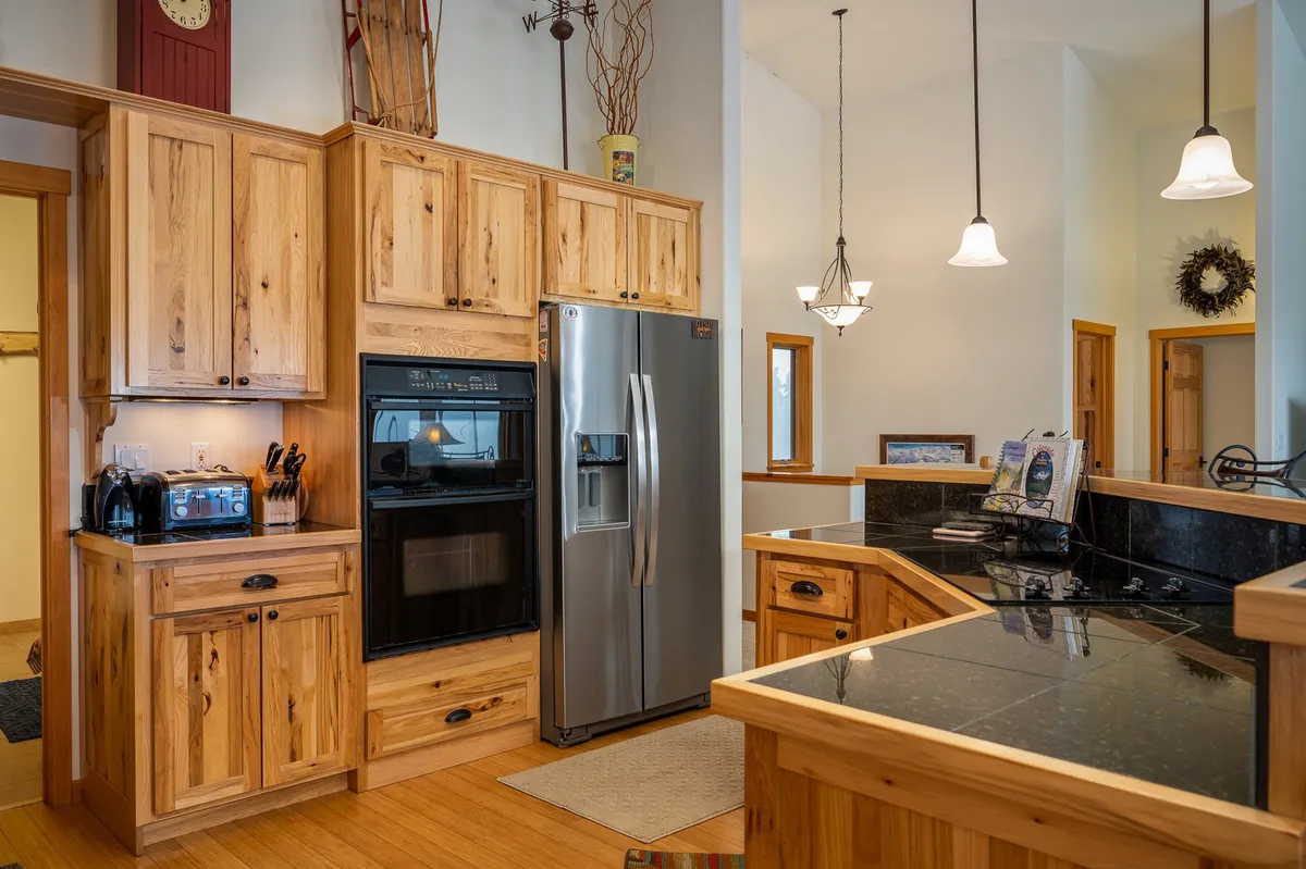 A bright, fully stocked kitchen with wooden cabinetry, stainless steel appliances, black countertops, and pendant lighting. The space looks spotless and ready for use, inviting guests to prepare gourmet meals or enjoy a cup of premium coffee.