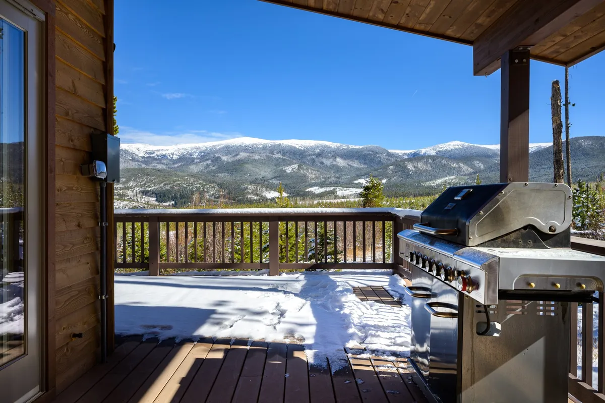An inviting exterior deck with a grill is shown, overlooking breathtaking mountain views and snow-dusted ground. The deck provides space for outdoor dining, relaxation, and social gatherings, ideal for enjoying sunset meals or early morning coffee in a scenic alpine setting.