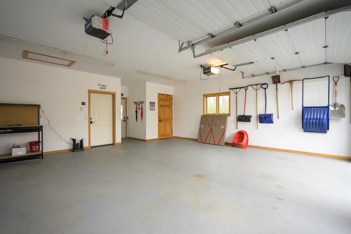 A practical and organized garage space featuring a visible garage door, a sturdy workbench lined with tools, and ample natural light from windows. The scene conveys readiness for adventure, with plenty of room for storing outdoor gear, bikes, or winter sports equipment.