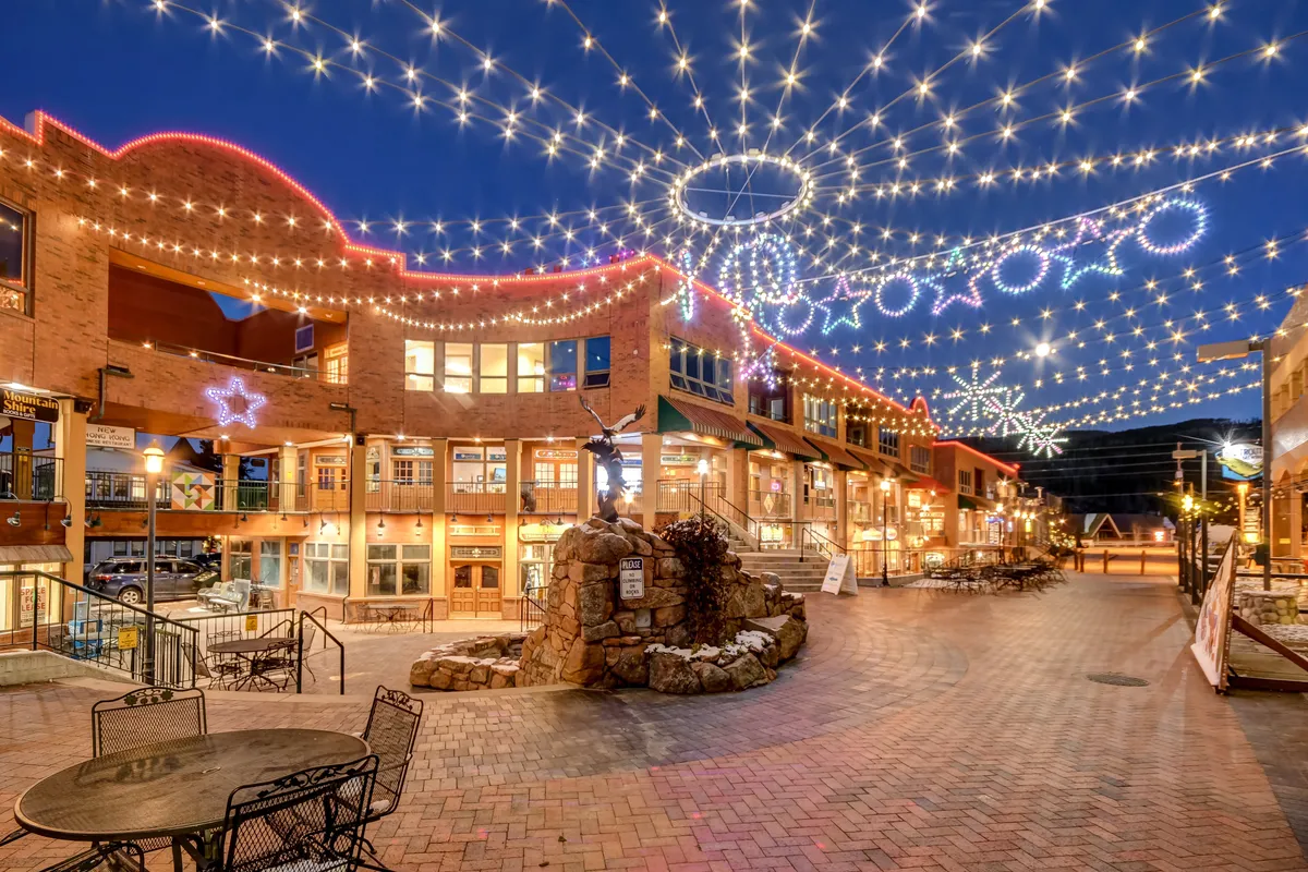 A lively exterior setting with string lights overhead, decorative stars, a stone fountain, and a brick walkway, inviting guests to dine, shop, or join community events under the stars.