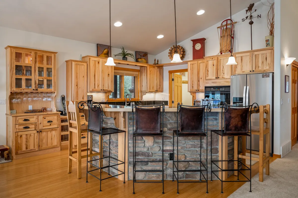A modern kitchen with a large island, warm wood cabinetry, stone accents, pendant lighting, and bar stools, designed for cooking, casual dining, and entertaining. The space is bright and welcoming, inviting group participation in meal prep and coffee breaks.