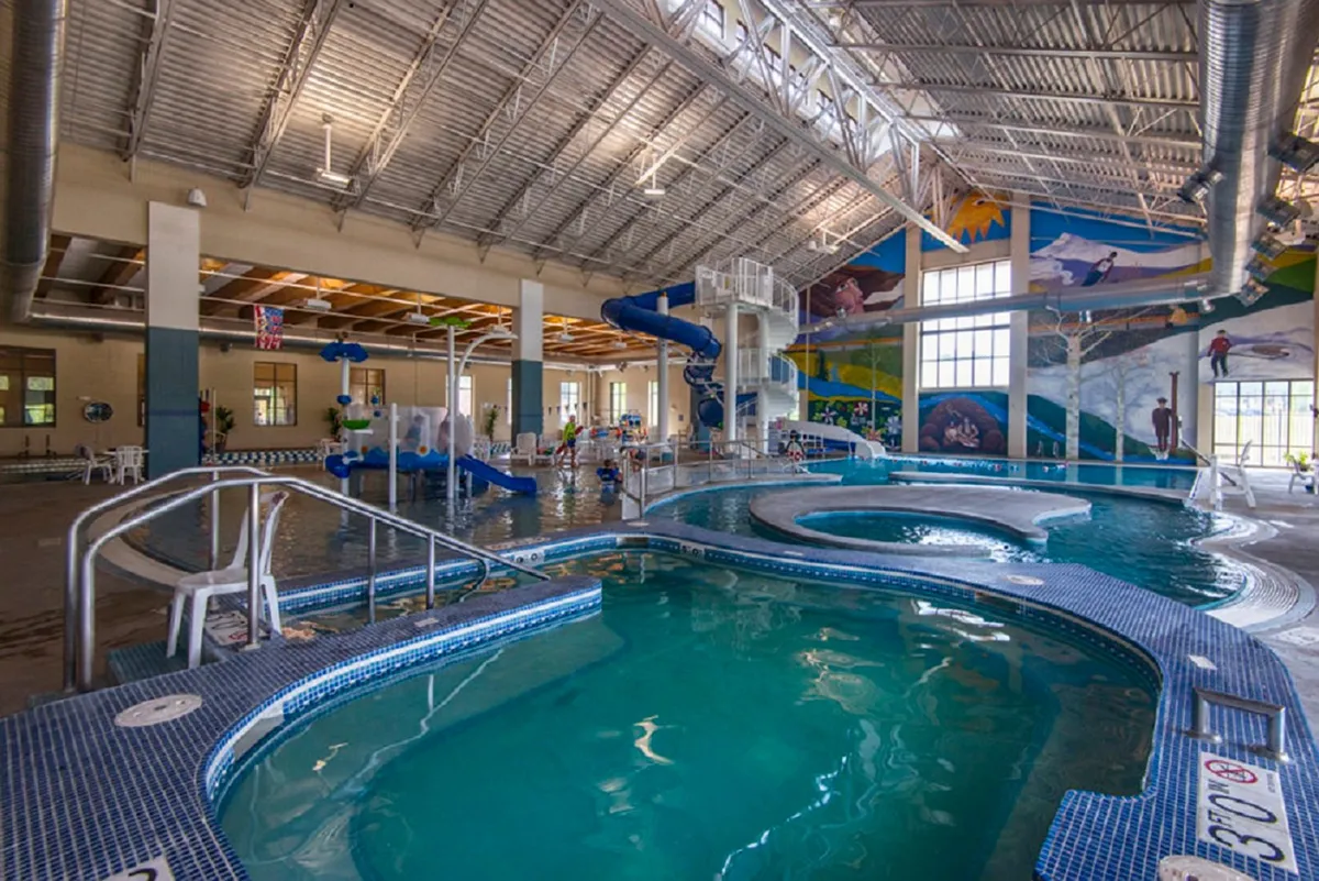 A colorful, energetic scene at a family-friendly recreation center, featuring water slides, children playing in pools, and vibrant murals. The lively atmosphere captures the fun and variety offered by the Grand Park Rec Center’s amenities.