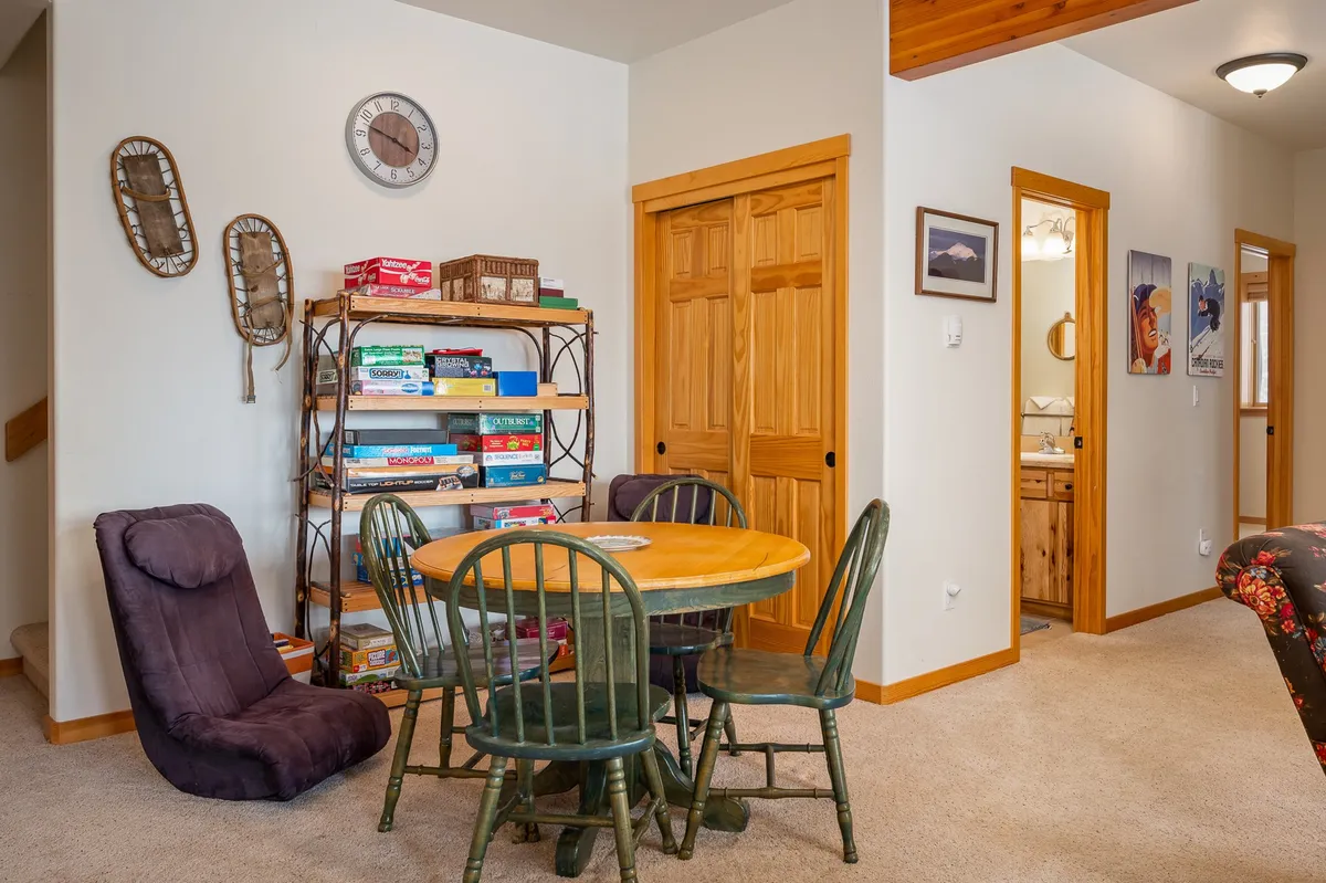 A cozy nook featuring a round wooden table with green chairs, shelves stacked with board games, and a comfy chair for relaxing. The space radiates warmth and invites family or friends to gather for game nights and casual conversation.